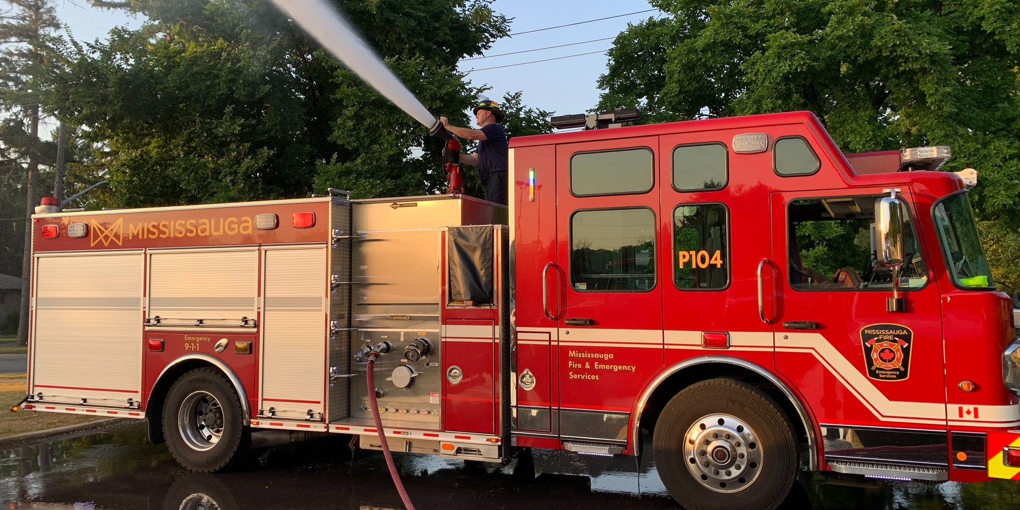 Firefighter spraying a hose of water from on top of a fire truck.